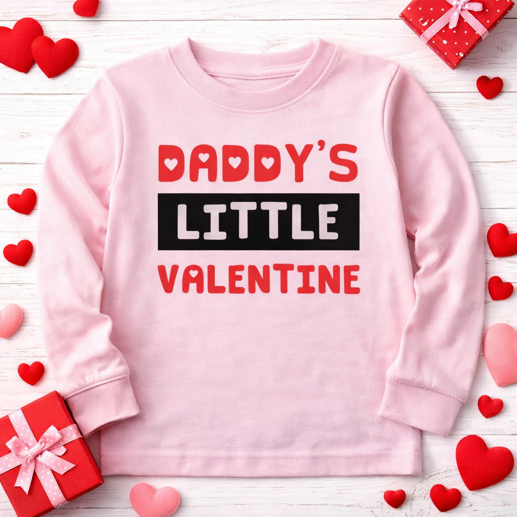 Pink sweatshirt with 'Daddy's Little Valentine' text on a wooden surface with heart decorations.